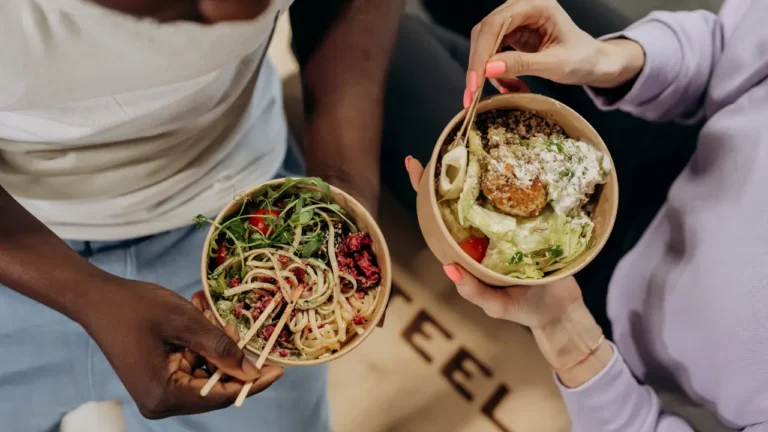 Two friends eating a bowl of noodles showing that all foods can fit in a healthy diet